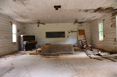 Country church sits abandoned and empty.  Antique, and ornate, piano has been left to disintegrate.  Old wooden pew is broken.  Sign hand printed on plywood says Hear my Prayer Lord Please. clipart