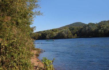 Two men fish the Boswell Shoals Launch Area on the White River, North Arkansas.  Ozark Mountains rise in front of them. clipart