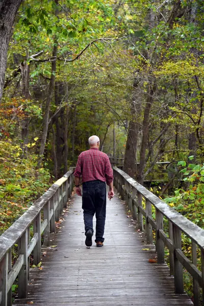 Stock image Elderly man takes the wooden walkway to the Mitchell's Mill Ruins in the Blanchard Springs Recreation Area in Northern Arkansas.  He has on a plaid shirt and black pants.