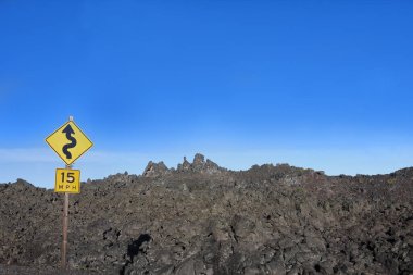 Sarı yol işareti, McKenzie Geçidi 'nde, Oregon' un merkezindeki kıvrımlar hakkında uyarıyor. Lav tarlası yol dışında yükseliyor..