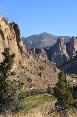 Oregon 'daki Smith Rock State Park' tan manzara, engebeli dağları ve uzak yaya köprüsünü ve patikalarını gösteriyor..