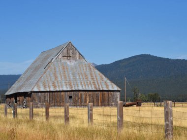 Oregon 'daki taşralı, ahşap ahır, sert kenarlı tahtalardan yapılmıştır. Teneke çatı paslanıyor. Çit ahırı sarmış..