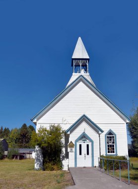 Beyaz ahşap kilise, mavi süslemeli, Oregon 'daki Fort Klamat Metodist Kilisesi' ne ev sahipliği yapıyor. Kilisenin teneke çatısı ve çan kulesi var.