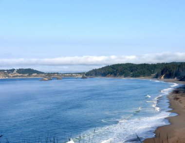 Port Orford Bay, in Oregon, has sea stacks and offshore islands.  Water and sky is blue. clipart