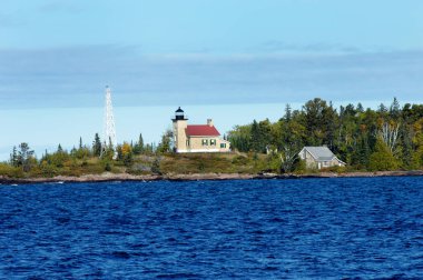 Automated light and historic Copper Harbor Lighthouse is visited by tourists.  Choppy waters of Lake Superior is deep blue and Fall colors shoreline. clipart