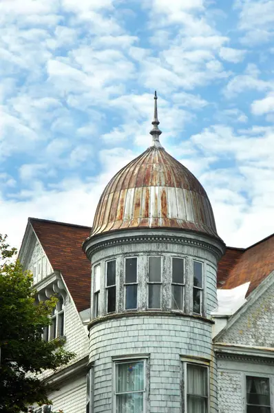 stock image Round tower has domed top and metal finial.  Home is white with shingled sides, paint peeling and broken window.  Home is located in Hancock, Michigan.