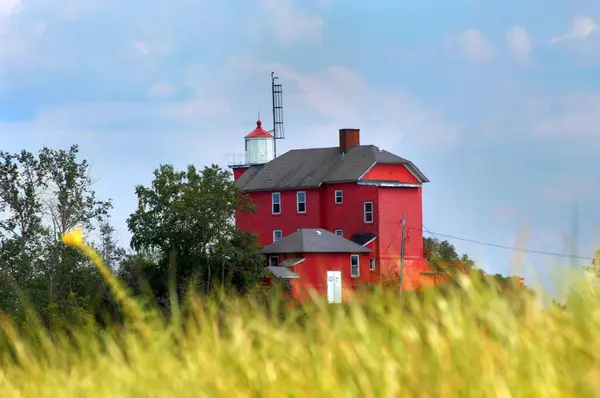 stock image Tall grass frames the Marquette Maritime Museum and Lighthouse in Marquette, Michigan.  Building is red, wooden and sits atop a wooden bluff overlooking Lake Superior.