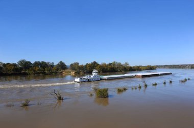 Tugboats get the job of moving and pushing cargo up and down the Mississippi.  This pusher is white and has a large load. clipart