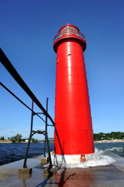 Mavi gökyüzü Michigan Gölü 'ndeki canlı kırmızı Grand Haven Deniz Feneri' ni çerçeveliyor. Dalgalar kulelerin tabanına vuruyor.