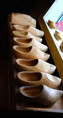 Row of carved wooden shoes sits on a shelf in front of a store window.  Store is in Nelis Dutch Village in Holland, Michigan. clipart