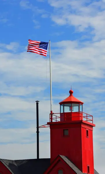 stock image Red tower of the Holland Harbor Lighthouse flies the American Flag.  Image shows lens and filial on top of light.