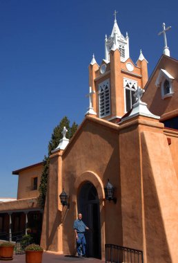 San Felipe de Neri Church is located on the square in Old Town, Albuquerque, New Mexico.  Male tourist stands at the door preparing to enter. clipart