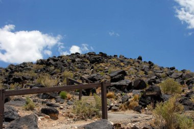 Kırsal ahşap raylar patikanın tepesine kadar uzanır. Petroglyphs yolu çiziyor ve tepesinde bir yürüyüşçü alçalmaya başlıyor..