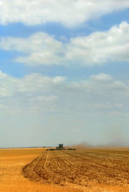 Çiftçi tarlalarını sürmek için uzun bir işe başlıyor. Mavi gökyüzü ve bulutlar alçaktan sarkır ve sabanın kanatlarından toz yükselir..