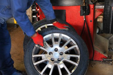 Lastik dükkanında çalışan bir işçi, tekerleğin kenarındaki krom jantları ovar ve parlatır. Kırmızı eldivenler giyiyor ve elinde bir bez parçası var..