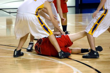 Boys player on basketball team hangs on for dear life.  He is on the floor and surrounded by the opposition. clipart