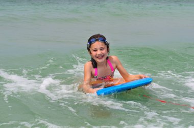 Florida, Madeira Sahili 'nde sörf tahtası sürmekten hoşlanan küçük kız kocaman bir gülümseme sergiliyor. Tahta mavi.