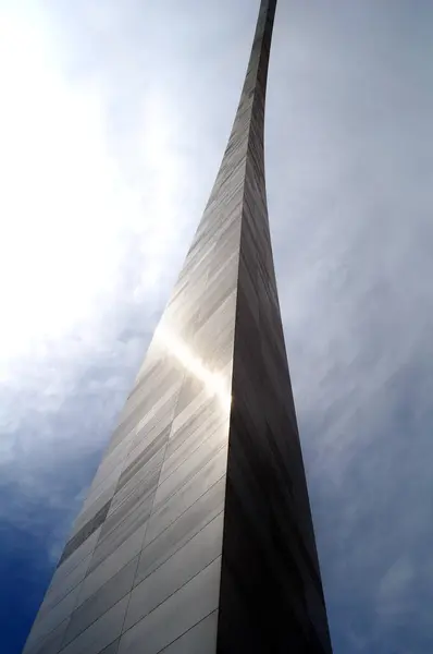 stock image Part of the Jefferson National Expansion Memorial, in St. Louis, Missouri, this inverted arch is covered in stainless steel.  It sits against clouds and blue sky.