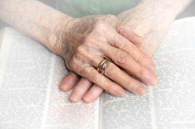 Eski eller açık bir İncil 'in üzerine tutunur. Elleri buruşmuş ve dünyanın dertleriyle yıpranmış..