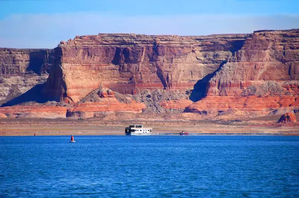 stock image Houseboat navigates the waters of Lake Powell.  Majestic sandstone cliffs form background.  Boats look tiny in comparison to the vertical sandstone behind them.