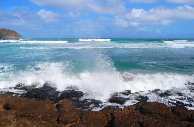 Dalgalar Hawaii 'deki Kauai Adası' nın kayalık kıyılarında süzülür. Gökyüzü mavi ve su turkuazdır. Ufuk mesafesi.