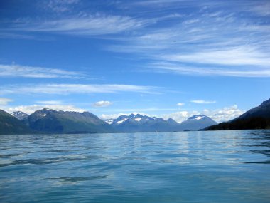 Alaska Valdez Körfezi 'ndeki dev Chugach Dağları' nın yanında küçük balıkçı gemileri de yüzüyor. Mavi gökyüzü ve mavi sular manzarayı dolduruyor.