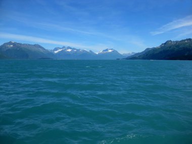 Uzak Chugach Dağları mavi gökyüzü ve suyla çevrilidir. Kar tepeleri zirveler.