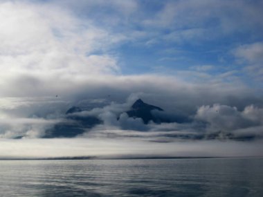 Sabah sisi, Alaska Valdez Körfezi üzerindeki Chugach Dağları 'nı kaplıyor. Mavi gökyüzü bulutları aşıyor.