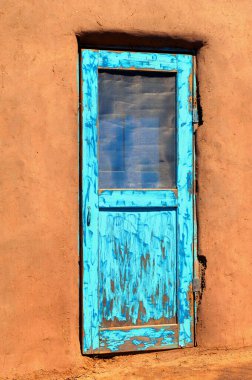 Taos, New Mexico yakınlarındaki tarihi ev, parlak turkuaz kapılı bir kerpiç. Boya soyuluyor ve soluyor..