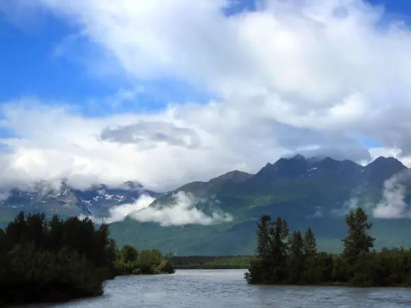 stock image Majestic Chugach Mountains tower over the Narrows of Valdez, Alaska.  Sky is powder blue and large clouds hover over the mountain peaks.