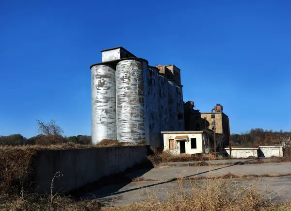 stock image Industrial buildings are closed and abandoned as this manufacturing facility has closed its doors.  Cylinder shaped storage bins are steel and beginning to rust.