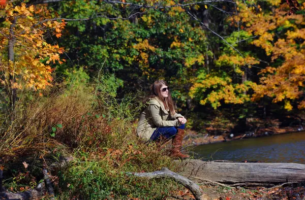 stock image Silence surrounds attractive young woman kneeling besides Poplar Tree Lake in Meeman Shelby Forest State Park.  Autumn colors her quiet world.