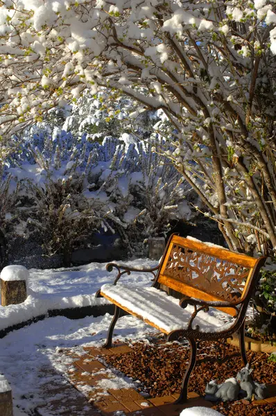 stock image Undisturbed snow covers bench seat in garden.  Winter snow covers tree and branches hanging overhead.