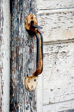 Kırsal ve paslı, kapı kolu yaşlanan beyaz bir kapıya tutunuyor. Ahşap çatlamış ve boya soyulmuş..