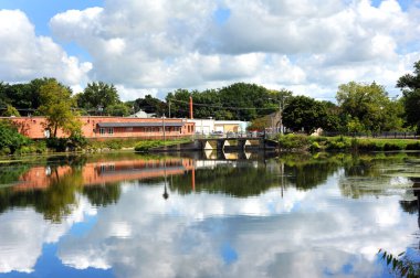 Stoughton Barajı, Yahara Nehri 'nin sakin ve huzurlu sularına yansıyor. Bu küçük Wisconsin kasabasında binalar, bulutlar ve mavi gökyüzü yansıyor..