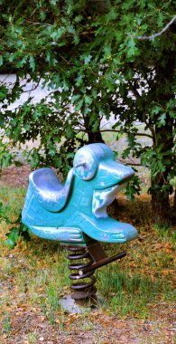 Klasik kurbağa, park, binicilik oyuncağı çocuk ağırlığı altında ileri geri sallanmak için desteklenir. Boya soyuluyor ve gri metal ortaya çıkıyor..