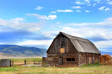Kırsal ahır ahşap çatılı ve bakımsız. Ahırın arkasındaki tarla Wyoming 'deki Cennet Vadisi' nin dağlarına doğru yuvarlanıyor..