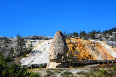 Visitors walk boardwalk and admire Liberty Cap at Mammoth Hot Springs in Yellowstone National Park. clipart