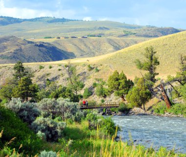 Kadın ve erkek, Yellowstone Ulusal Parkı 'ndaki Gardner Nehri' ni geçen yaya köprüsüne yaslanıyor. Köprü tahta..