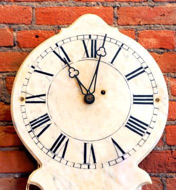 Saat suratı, kırsal bir kırmızı tuğla duvarın karşısında duruyor. Roma rakamları ve metal eller saat 11 yönünde..