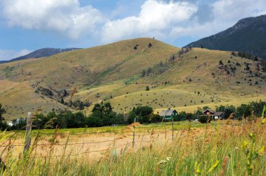 Absaroka Dağları 'nın eteklerinde yeşil ahır ve çiftlik görülür. Çit ve uzun çim görüntünün uzunluğu.