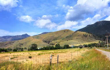 Green barn and farm sit at the foothills of the Absaroka Mountains in Montana.  Rustic fence and road lead toward homestead. clipart