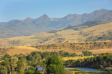 Happy Valley, Montana is highlighted by the evening sky.  Lone home sits nestled in the trees besides the Yellowstone River. clipart