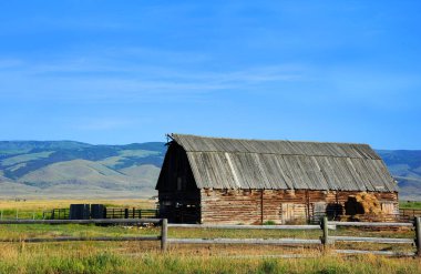 Ahşap çatılı ahır Happy Valley, Montana 'da. Dağlar ve mavi gökyüzü arkaplan oluşturur.