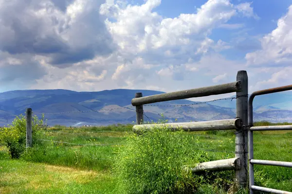 stock image Gallatin Mountains are covered in clouds.  Rustic wooden fence runs length of image seperating meadow and mountains.