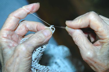 Yaşlı eller dantel örgü örüyorlar. Derisi buruşuk, elleri buruşuk. Elleri hayatı boyunca çok çalıştı..