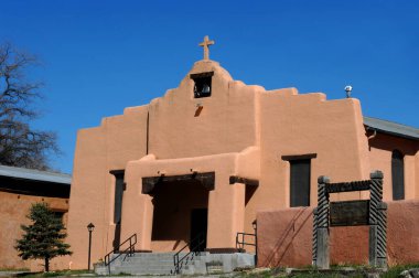 Aging Saint Anthony Church in Dexon, New Mexico has bell tower and crumbling cross steeple.  Stucco building with wooden sign. clipart