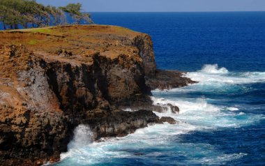 Büyük Hawaii Adası 'nın kuzey ucundaki engebeli uçurumlar Alenuihaha Kanalı' ndaki dalgalı denizleri görüyor. Su gök mavisi renginde ve kayalıklar koyu kırmızı bir kil ile kaplıdır..