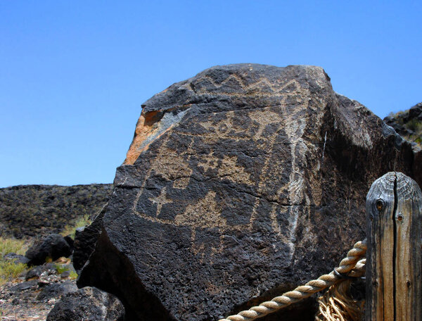 Large basalt rock has Pueblo Indian petroglyph.  Roped trail leads through one of the trail options in the Petroglyph National Monument in Albuquerque, New Mexico.