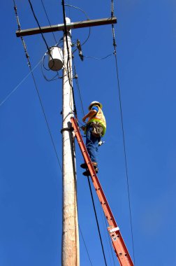 Tamirci, yüksek bir telefon direğindeki telefon ve kablo hatlarında çalışır. 30 metrelik bir merdivenin üzerinde duruyor ve emniyet kemeri, güvenlik yeleği ve kaskı takıyor..
